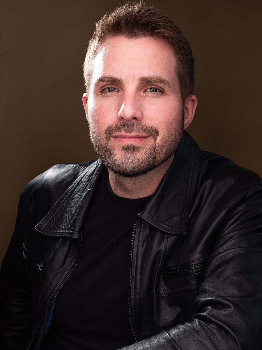 Scott Squire in a black leather jacket against a warm brown backdrop
