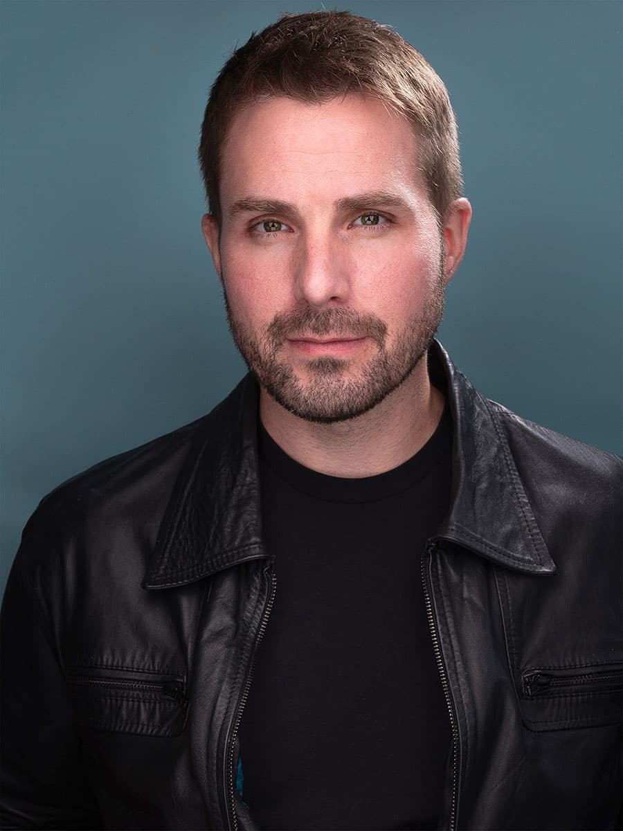 Scott Squire in a black leather jacket against a blue backdrop